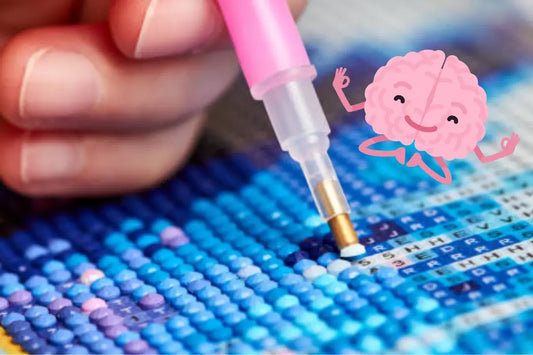Close-up van een hand die met een roze diamond painting pen blauwe steentjes plaatst op een canvas. Toegevoegd is een illustratie van een vrolijk brein.