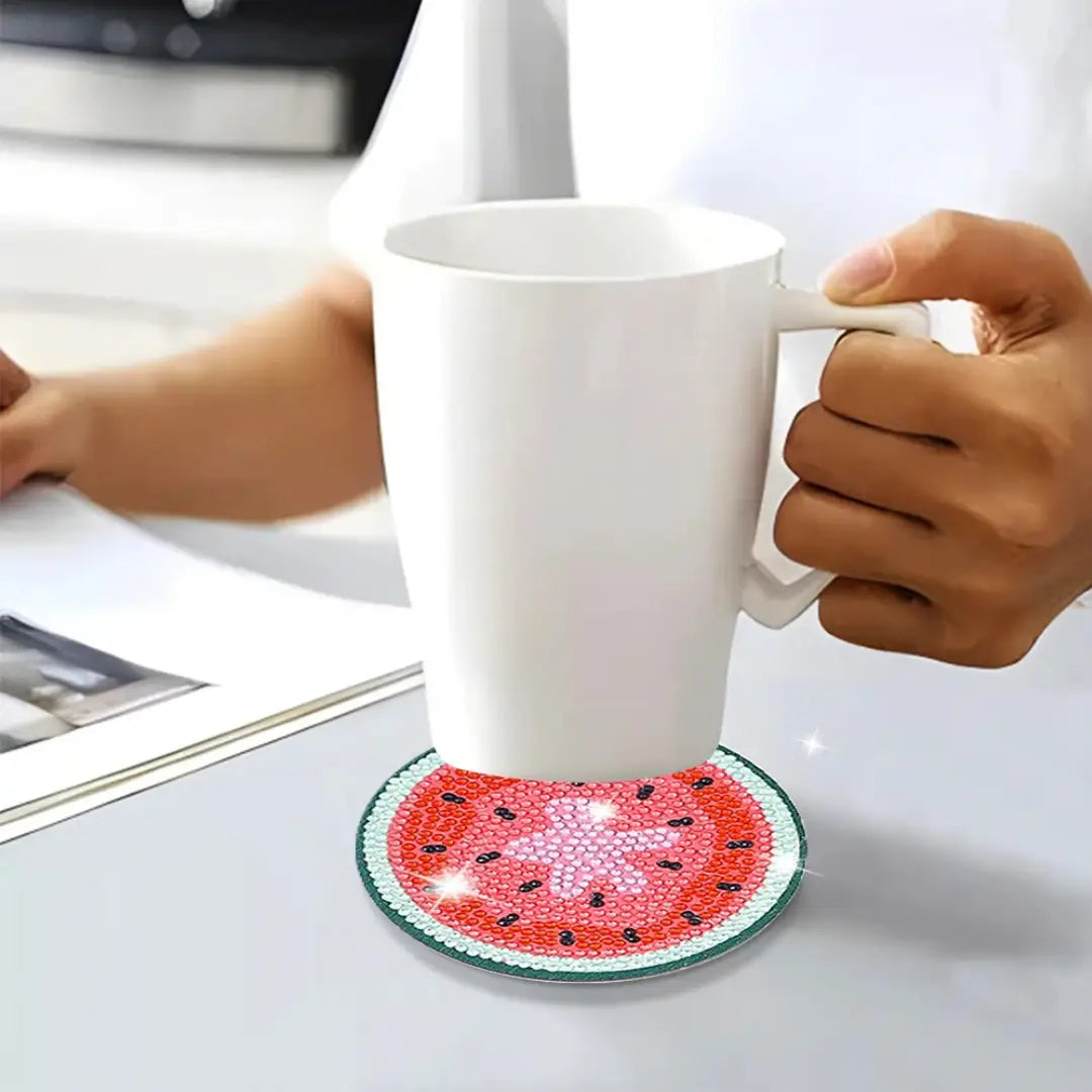 Diamond painting onderzetters met kleurrijke fruitmotieven onder een kop koffie op een tafel.