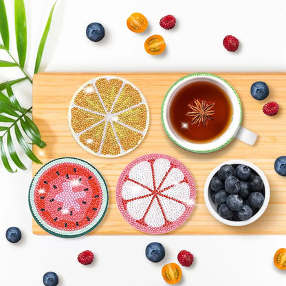 Vier diamond painting onderzetters in fruitdesigns, gepresenteerd op een houten plank met thee en bessen.