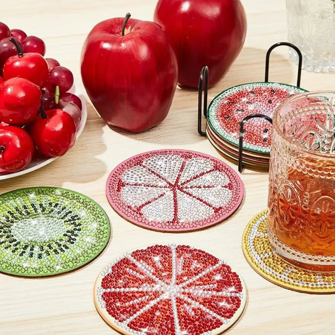 Fruitvormige diamond painting onderzetters, inclusief kiwi en grapefruit, met een glas sap op een tafel.
