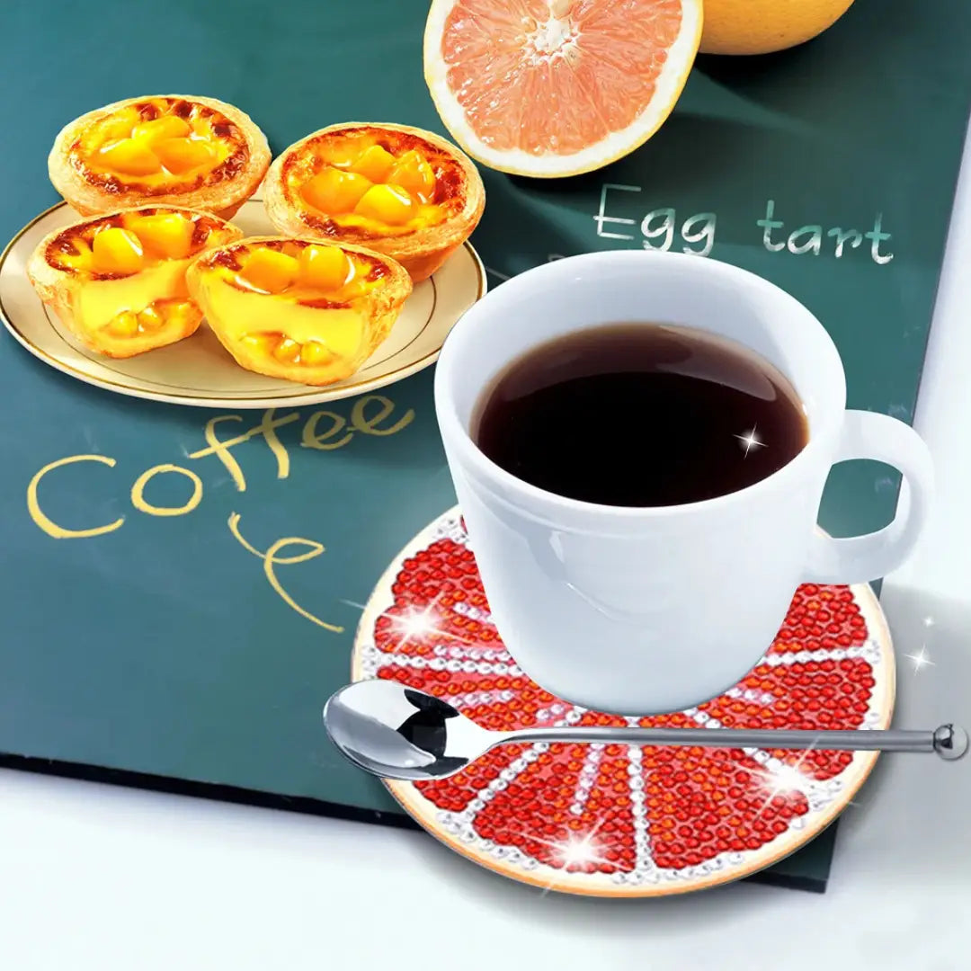 Diamond painting onderzetter met grapefruit design onder een kop koffie, met taart en citrus op de achtergrond.