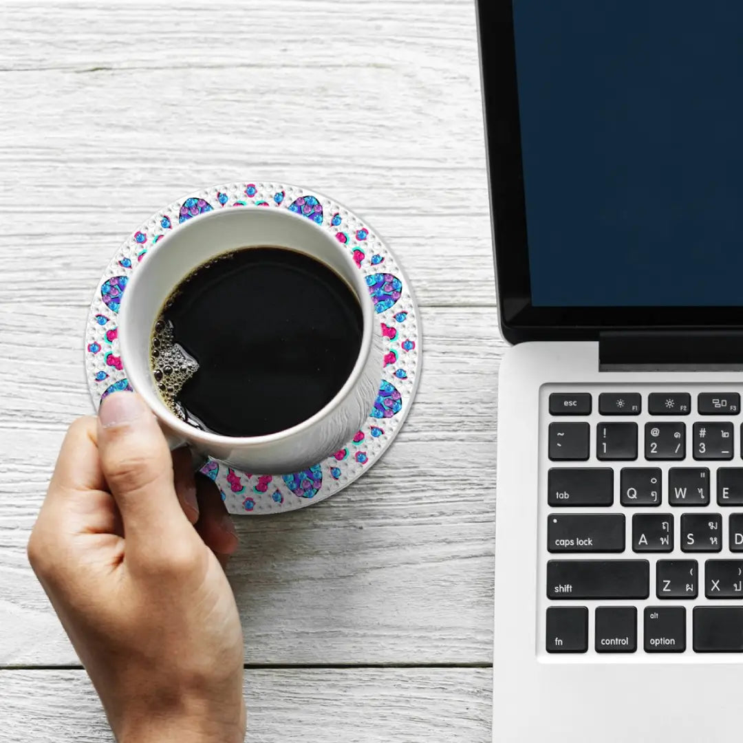 Een kop zwarte koffie op een mandala diamond painting onderzetter naast een laptop op een witte houten tafel.