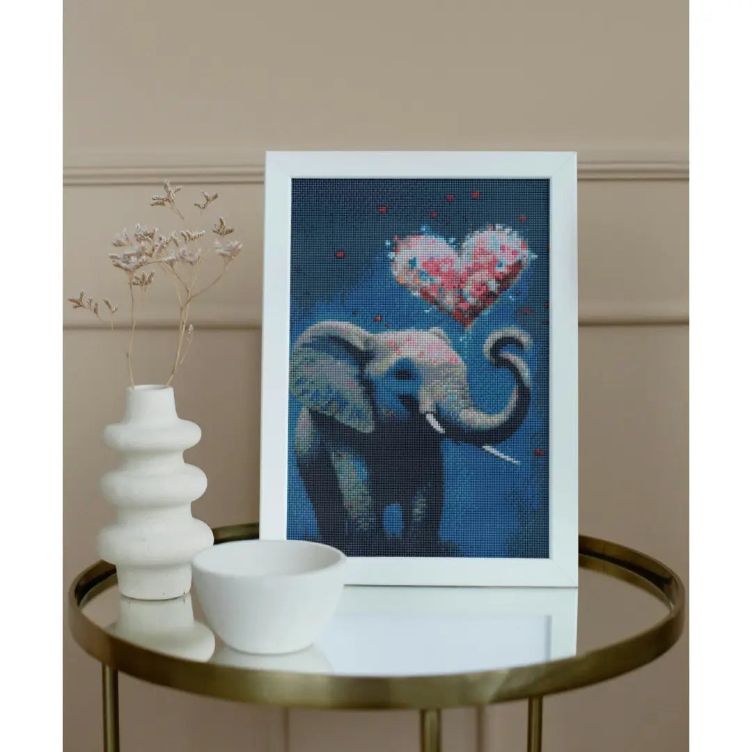 Diamond painting van een olifant met een hartvormige ballon, geplaatst op een ronde tafel met een witte vaas en een kom.