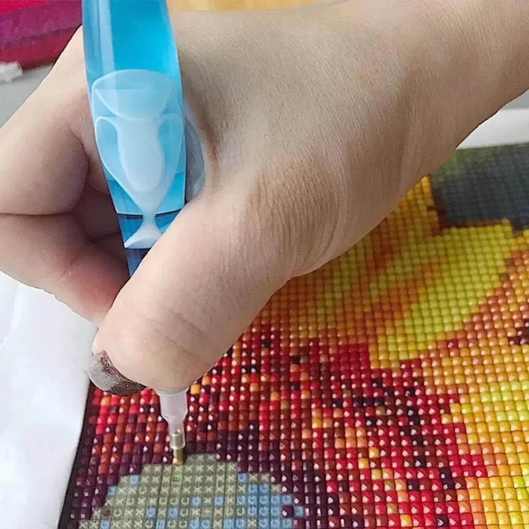 Hand gebruikt een blauwe pen om kleine, kleurrijke steentjes op een diamond painting canvas te plaatsen.