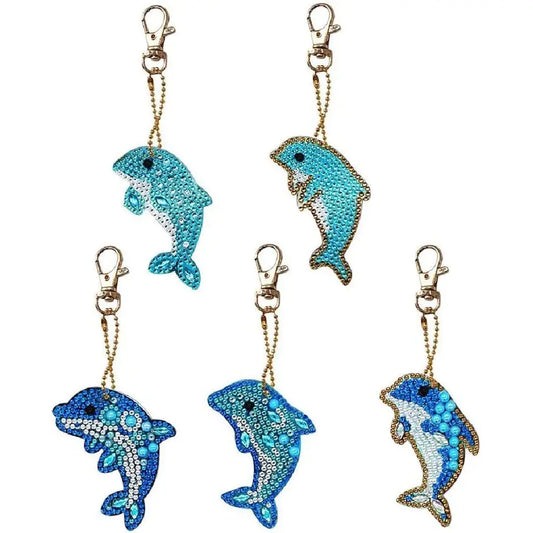 Verscheidenheid aan diamond painting sleutelhangers in de vorm van dolfijnen in levendige blauwe kleuren.